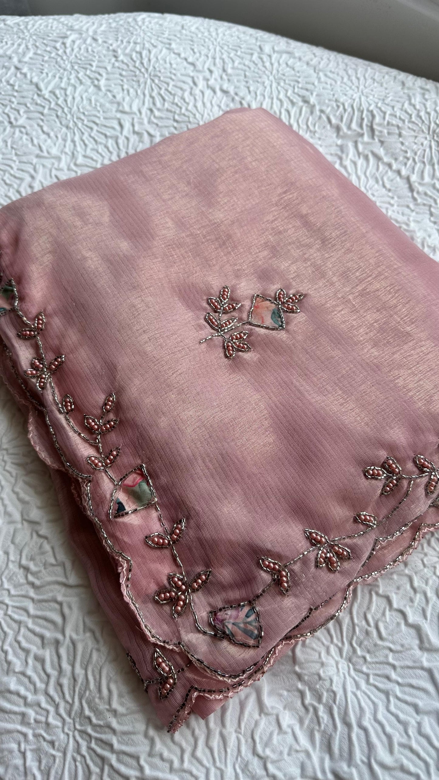 Embroidered pastel pink saree detail showing floral vine border and scattered motifs.