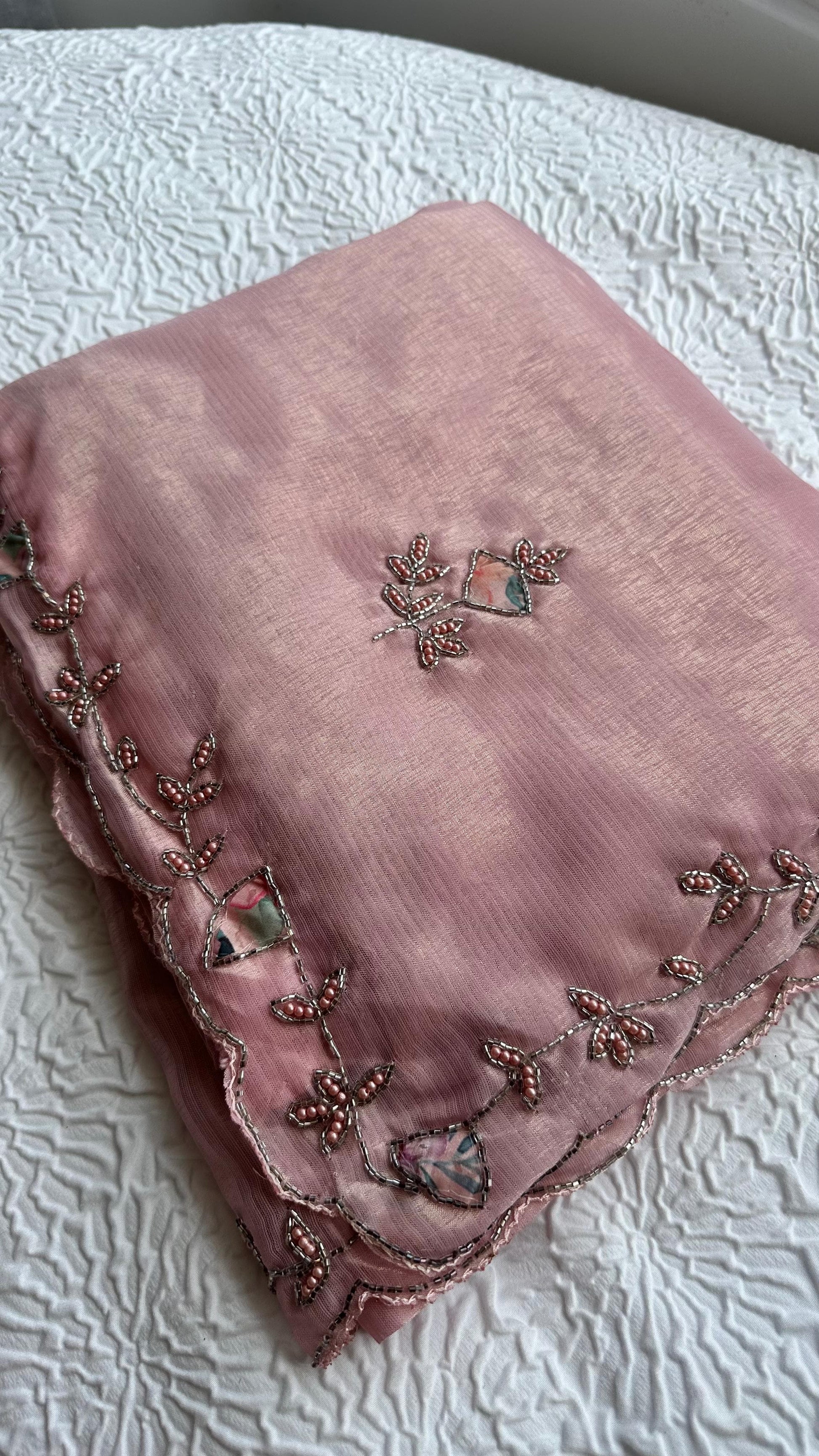 Embroidered pastel pink saree detail showing floral vine border and scattered motifs.