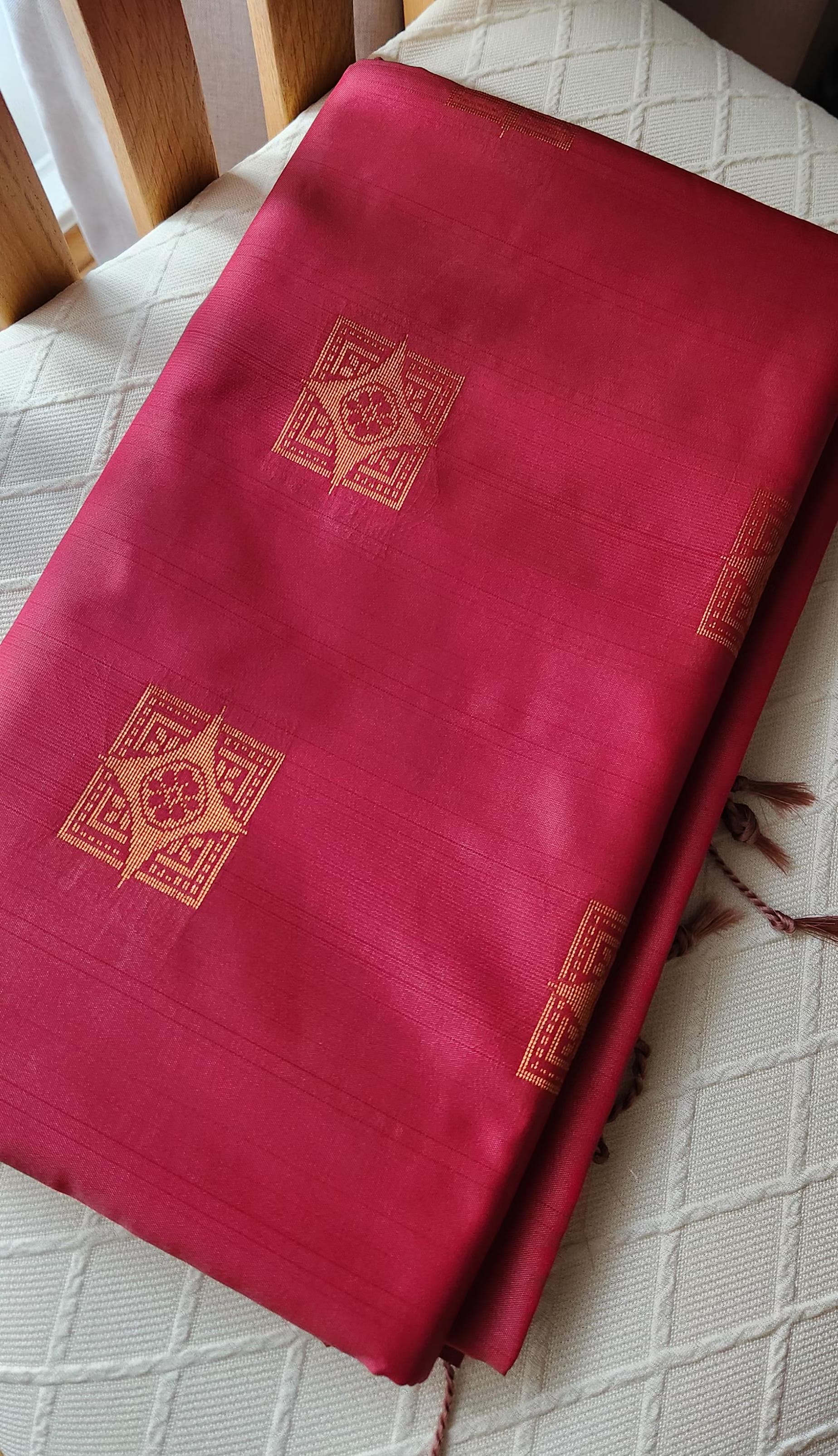 Deep pink soft silk saree with gold zari motifs and geometric woven pallu, displayed folded with tassels for festive and traditional wear.