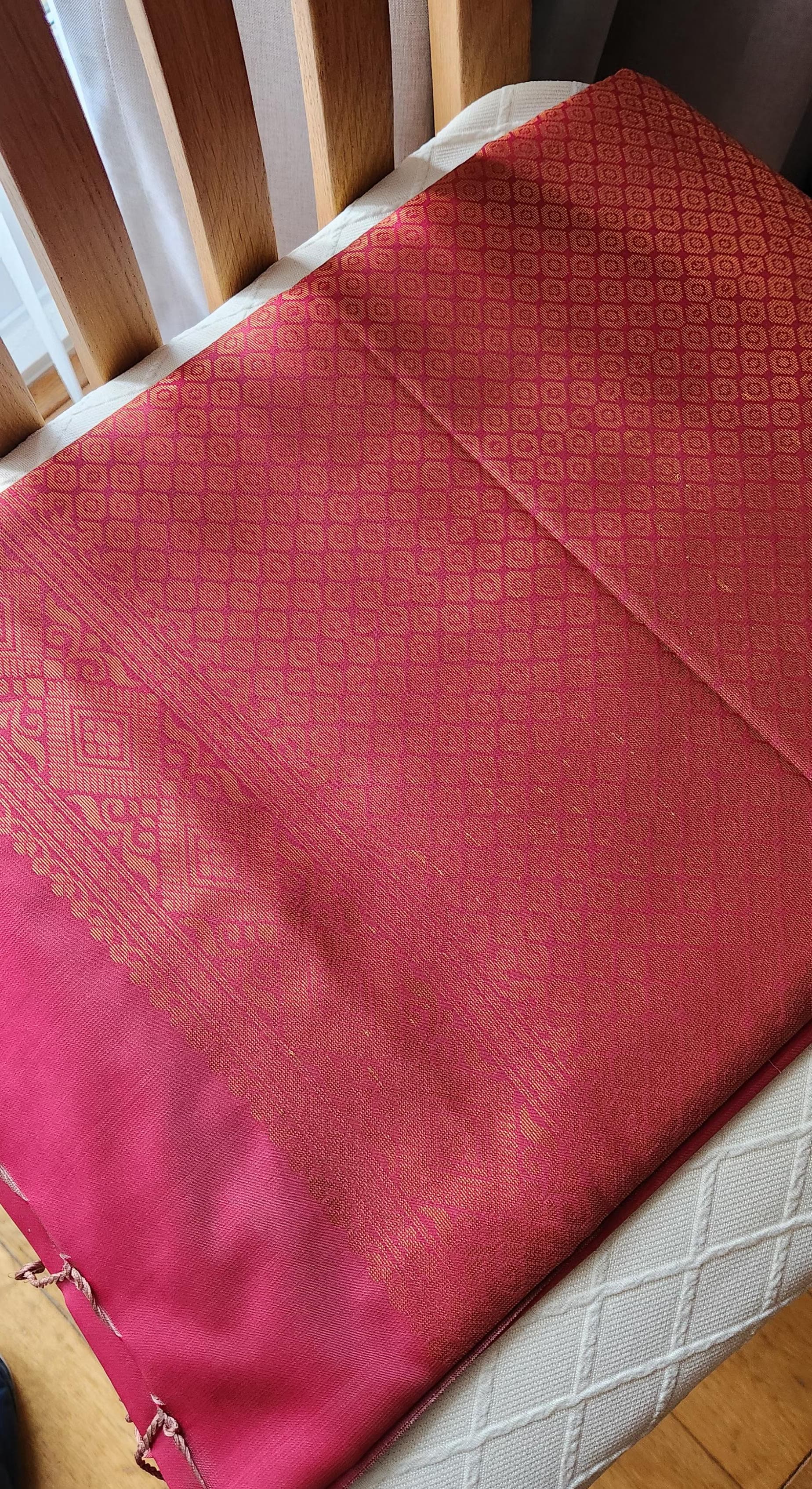 Deep pink soft silk saree with gold zari motifs and geometric woven pallu, displayed folded with tassels for festive and traditional wear.
