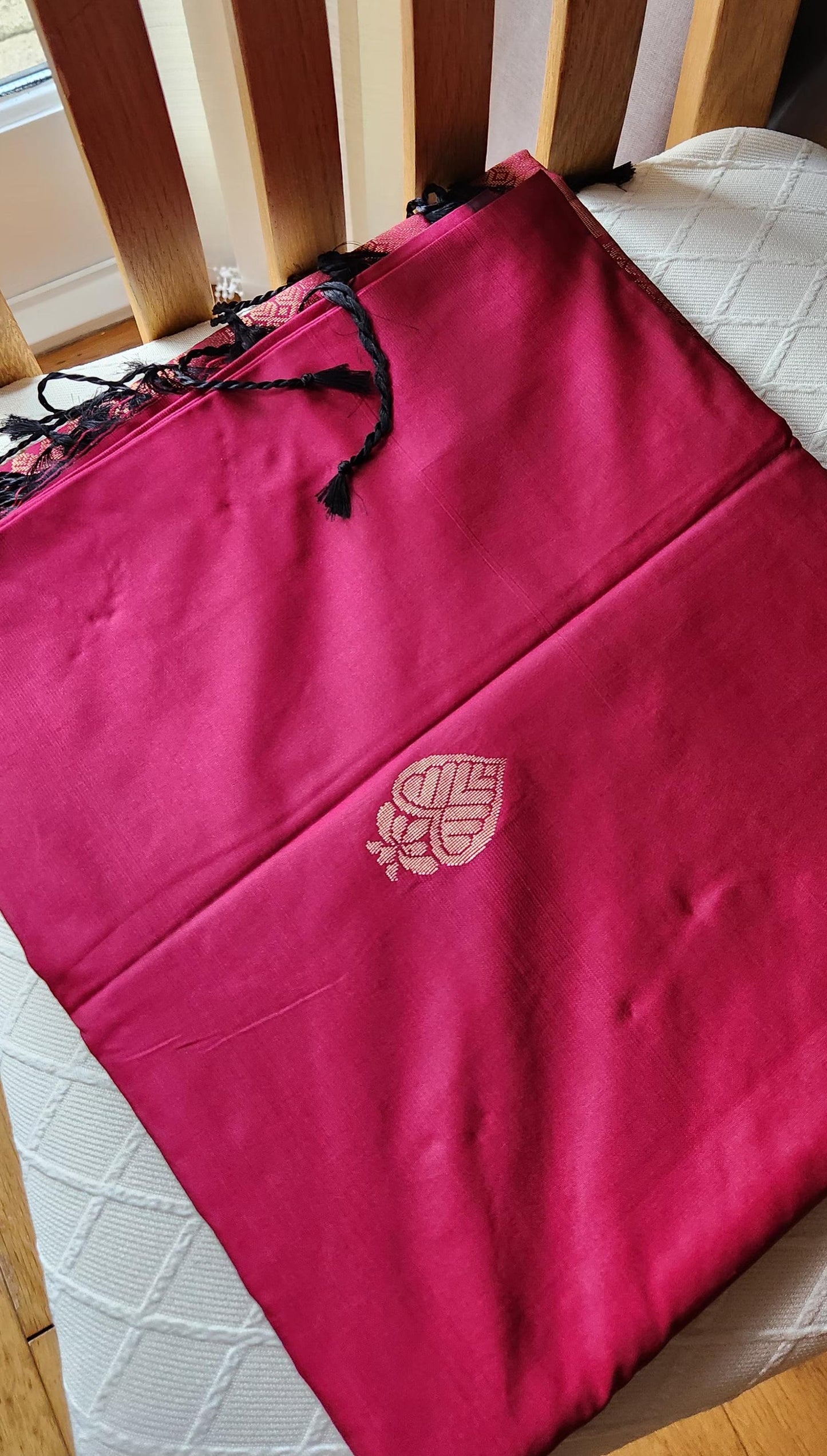 Rani pink soft silk saree with geometric zari weaving and floral zari border displayed folded on a white textured surface