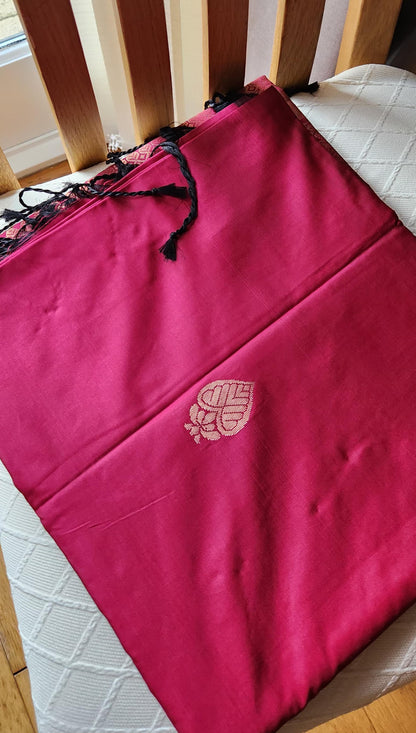 Rani pink soft silk saree with geometric zari weaving and floral zari border displayed folded on a white textured surface