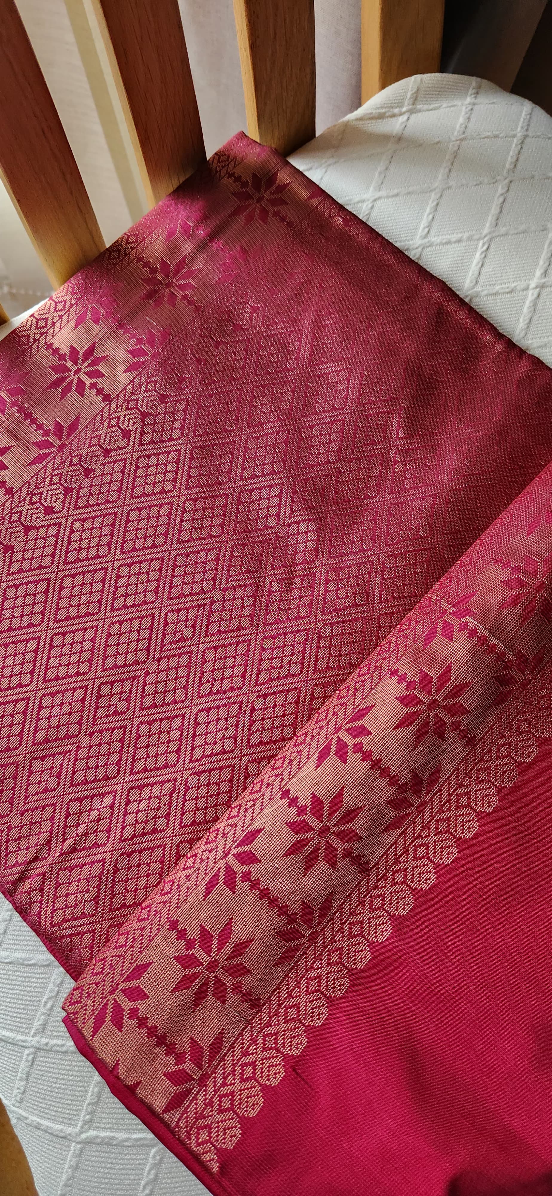 Rani pink soft silk saree with geometric zari weaving and floral zari border displayed folded on a white textured surface