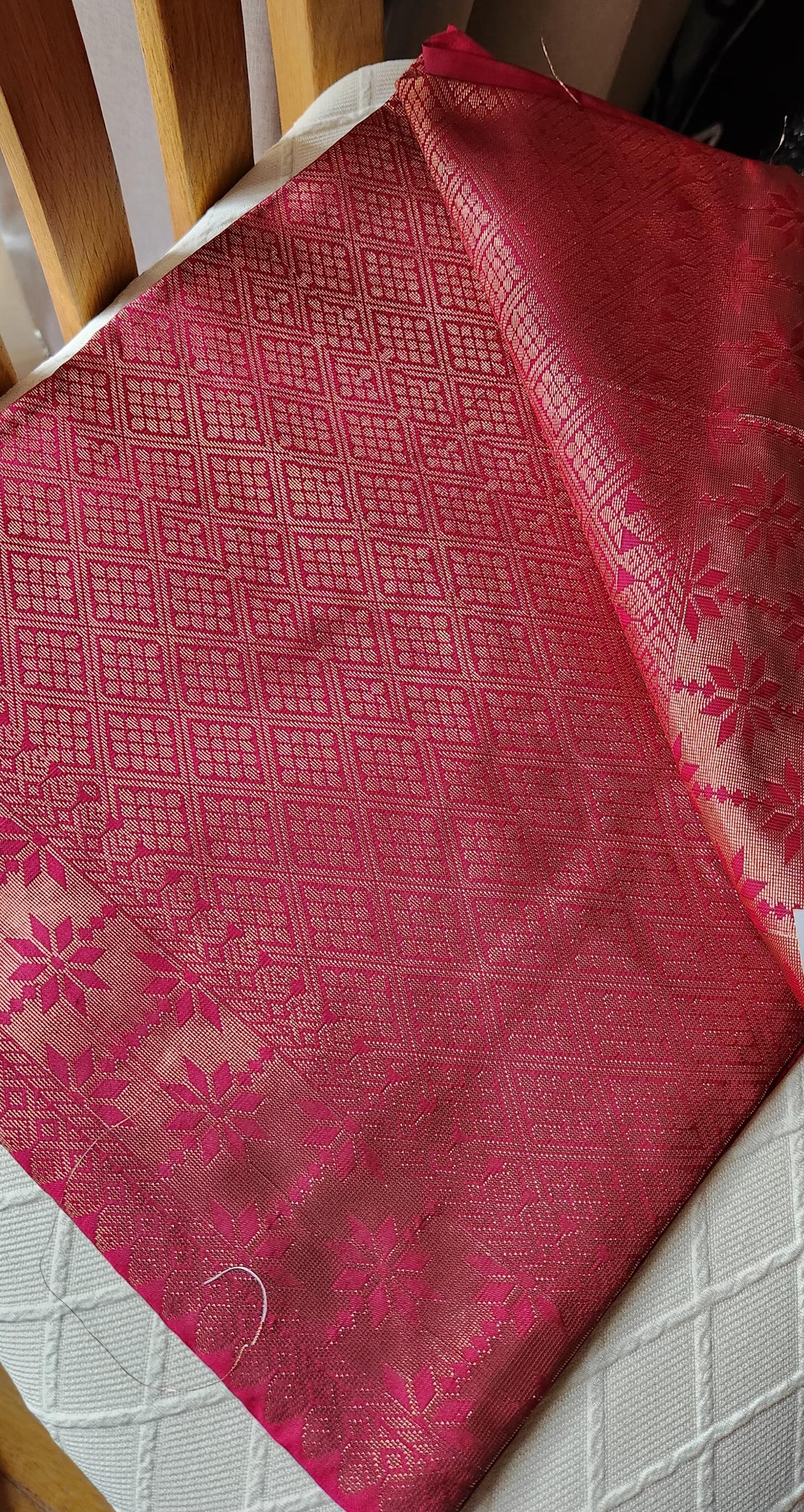 Rani pink soft silk saree with geometric zari weaving and floral zari border displayed folded on a white textured surface