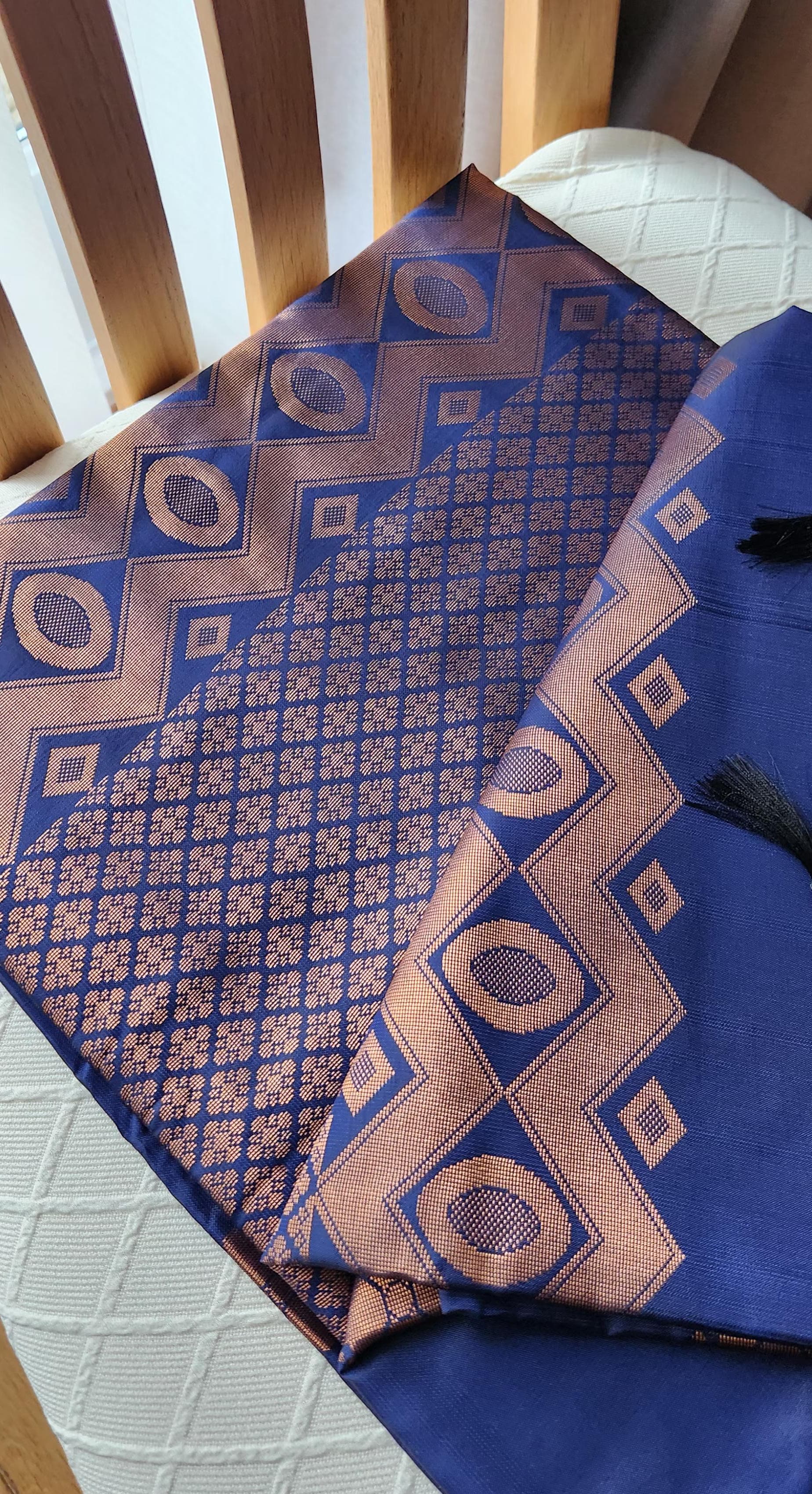 Navy blue soft silk saree with gold zari motifs, geometric woven border, and traditional pallu with tassels displayed on a light background.