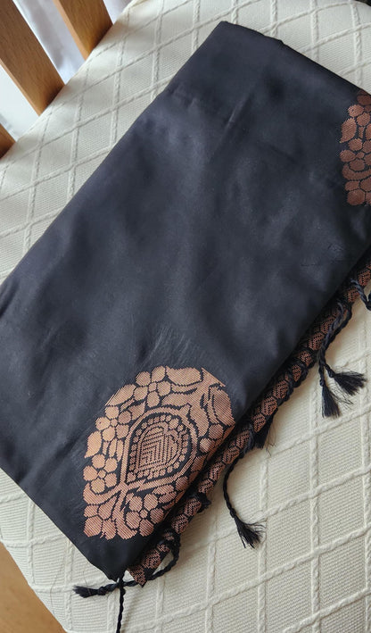 Charcoal black soft silk saree with antique copper zari motifs and traditional woven border displayed on a light fabric background