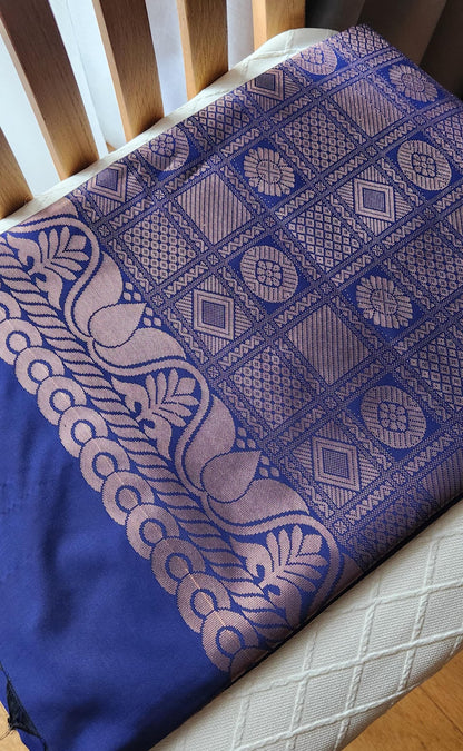 Deep navy blue silk saree with antique gold zari floral buttas and black tassels laid flat