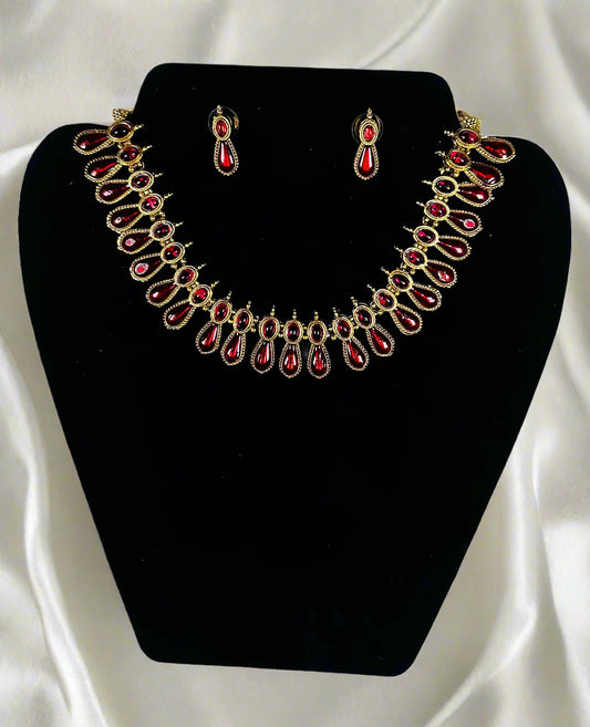 Antique gold ruby teardrop necklace and earrings jewelry set with Victorian style ornate metalwork displayed on black velvet stand