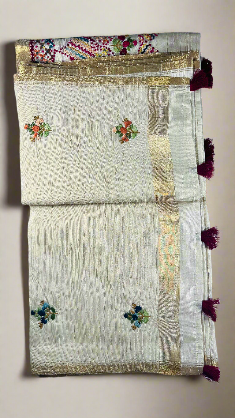 Off-white semi tussar silk saree with multicolor Resham thread embroidery, golden zari border, and maroon tassels.
