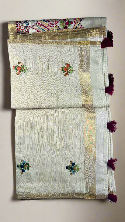Off-white semi tussar silk saree with multicolor Resham thread embroidery, golden zari border, and maroon tassels.
