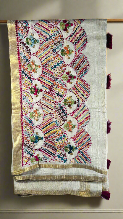 Off-white semi tussar silk saree with multicolor Resham thread embroidery, golden zari border, and maroon tassels.
