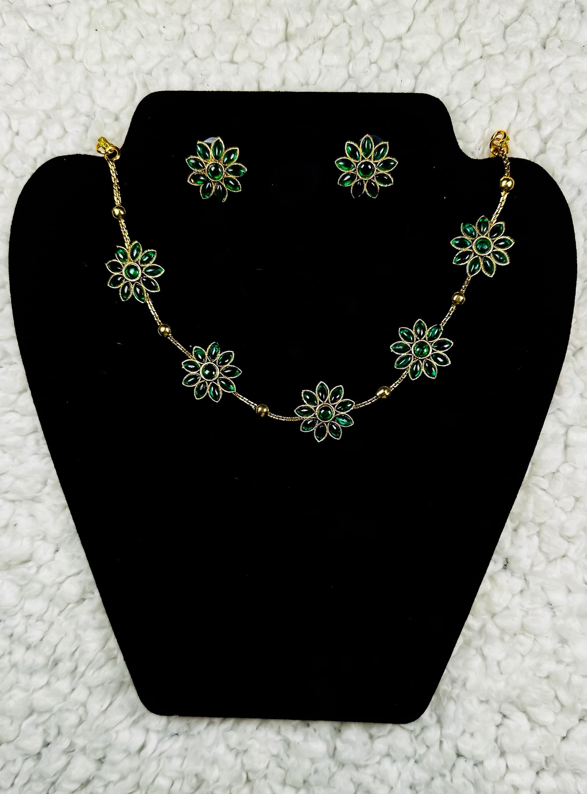 Delicate gold flower necklace and earrings jewelry set with emerald green petals in botanical station design displayed on black velvet stand