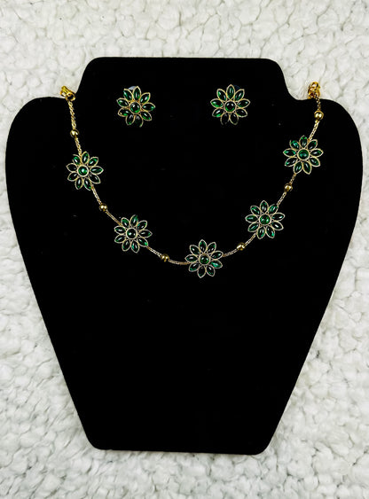 Delicate gold flower necklace and earrings jewelry set with emerald green petals in botanical station design displayed on black velvet stand