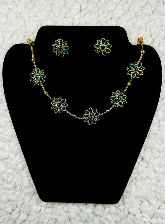 Delicate gold flower necklace and earrings jewelry set with emerald green petals in botanical station design displayed on black velvet stand