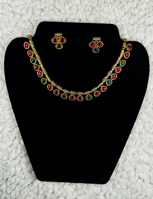 Gold collar necklace and earrings jewelry set with multicolor ruby red and emerald green teardrop stones in statement design displayed on black velvet stand