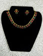 Gold collar necklace and earrings jewelry set with multicolor ruby red and emerald green teardrop stones in statement design displayed on black velvet stand