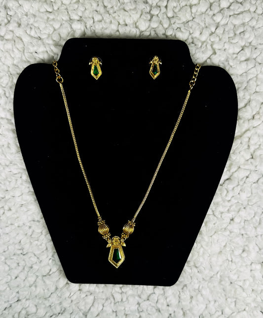 Gold plated geometric necklace and earrings jewelry set with emerald green diamond-shaped pendants displayed on black velvet jewelry stand
