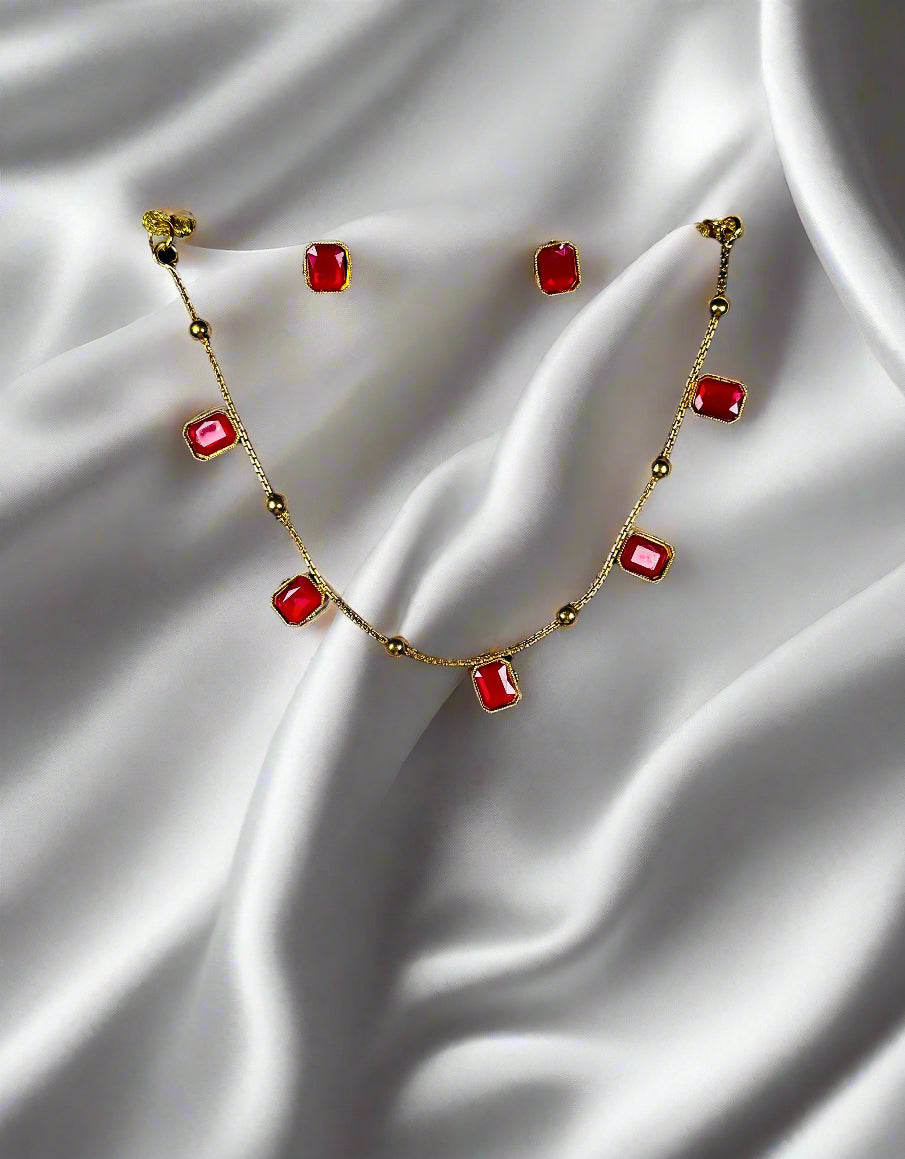 Gold station necklace and earrings jewelry set with rectangular ruby red stones in minimalist geometric design displayed on black velvet stand