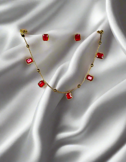 Gold station necklace and earrings jewelry set with rectangular ruby red stones in minimalist geometric design displayed on black velvet stand