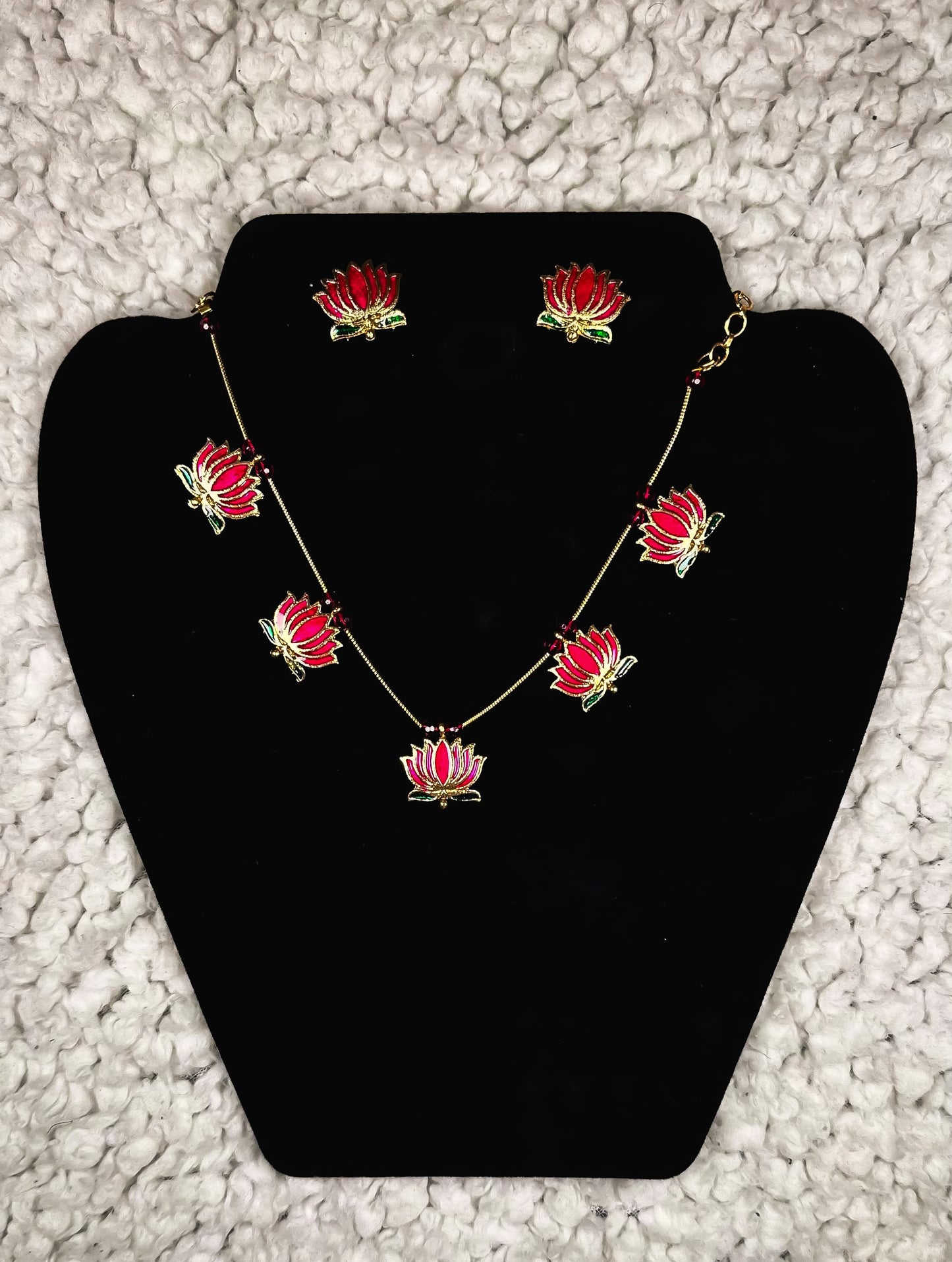 Red lotus flower jewelry set with gold-plated necklace and matching stud earrings displayed on black velvet jewelry display stand