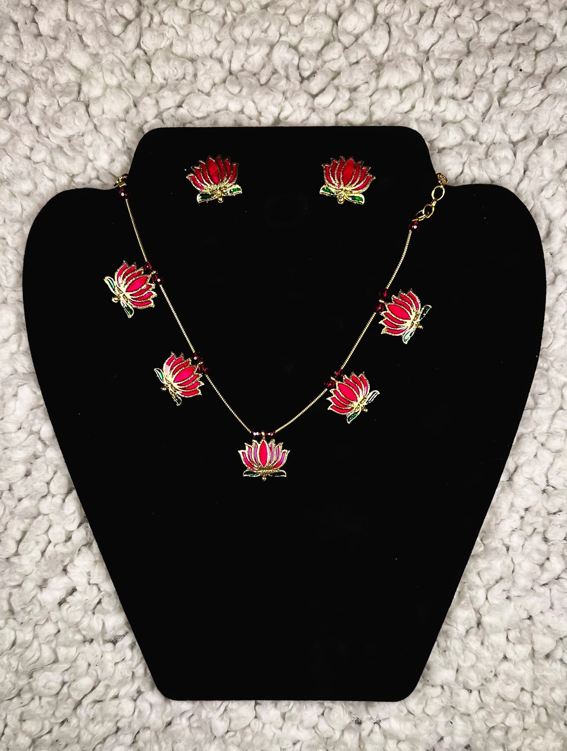 Red lotus flower jewelry set with gold-plated necklace and matching stud earrings displayed on black velvet jewelry display stand