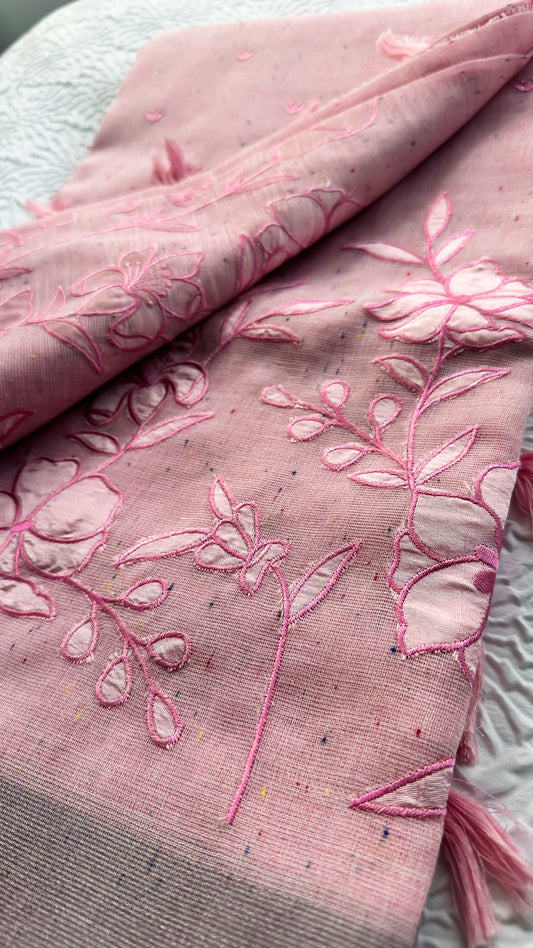 Soft pink linen saree with floral appliqué embroidery, speckled pattern, grey border, and pink tassels.