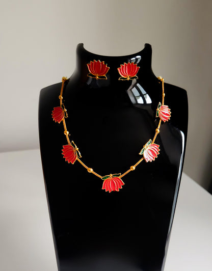 Red lotus enamel necklace with golden beads and matching earrings on black display.
