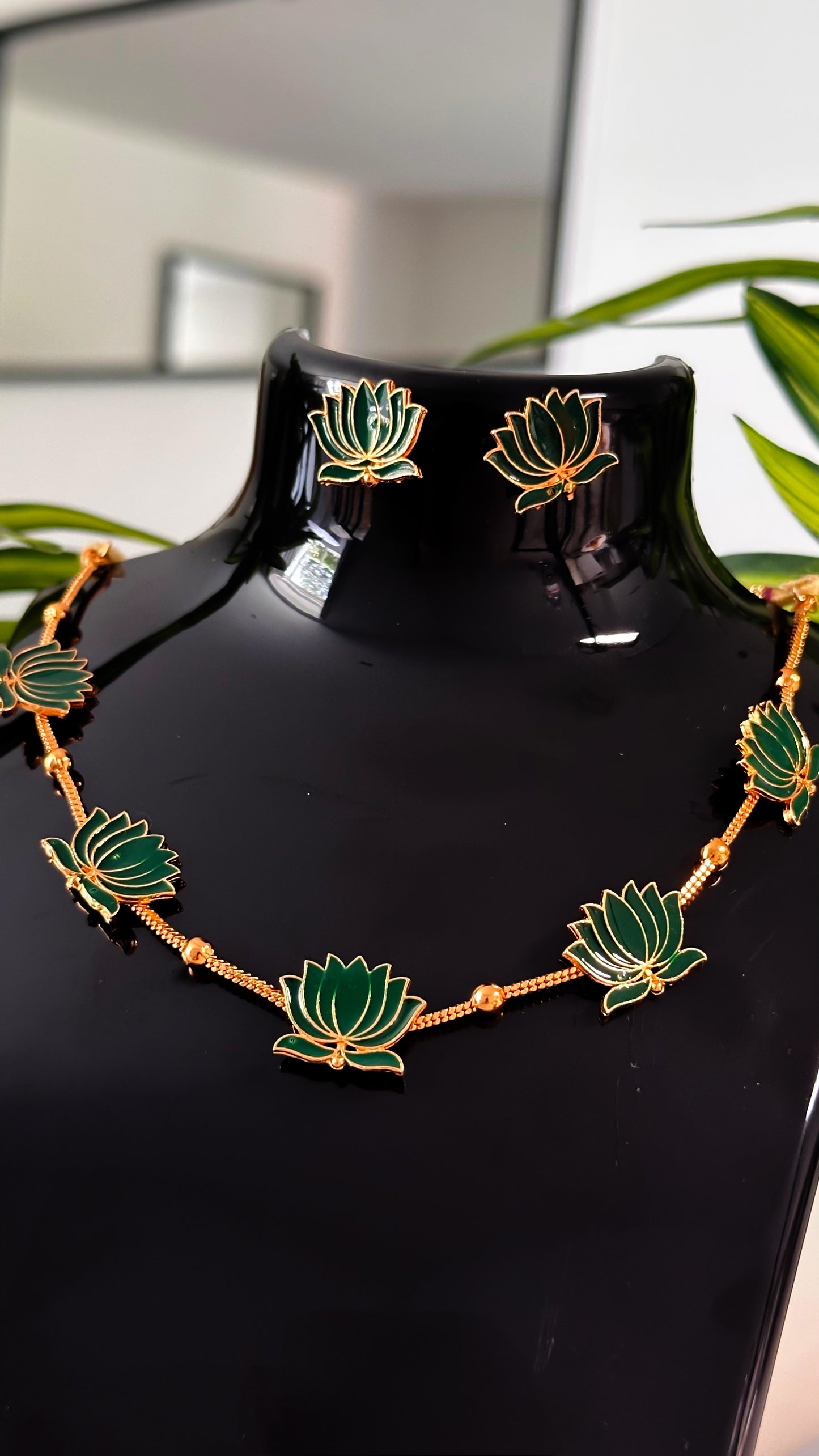Green lotus enamel necklace with golden detailing and matching earrings on black display.