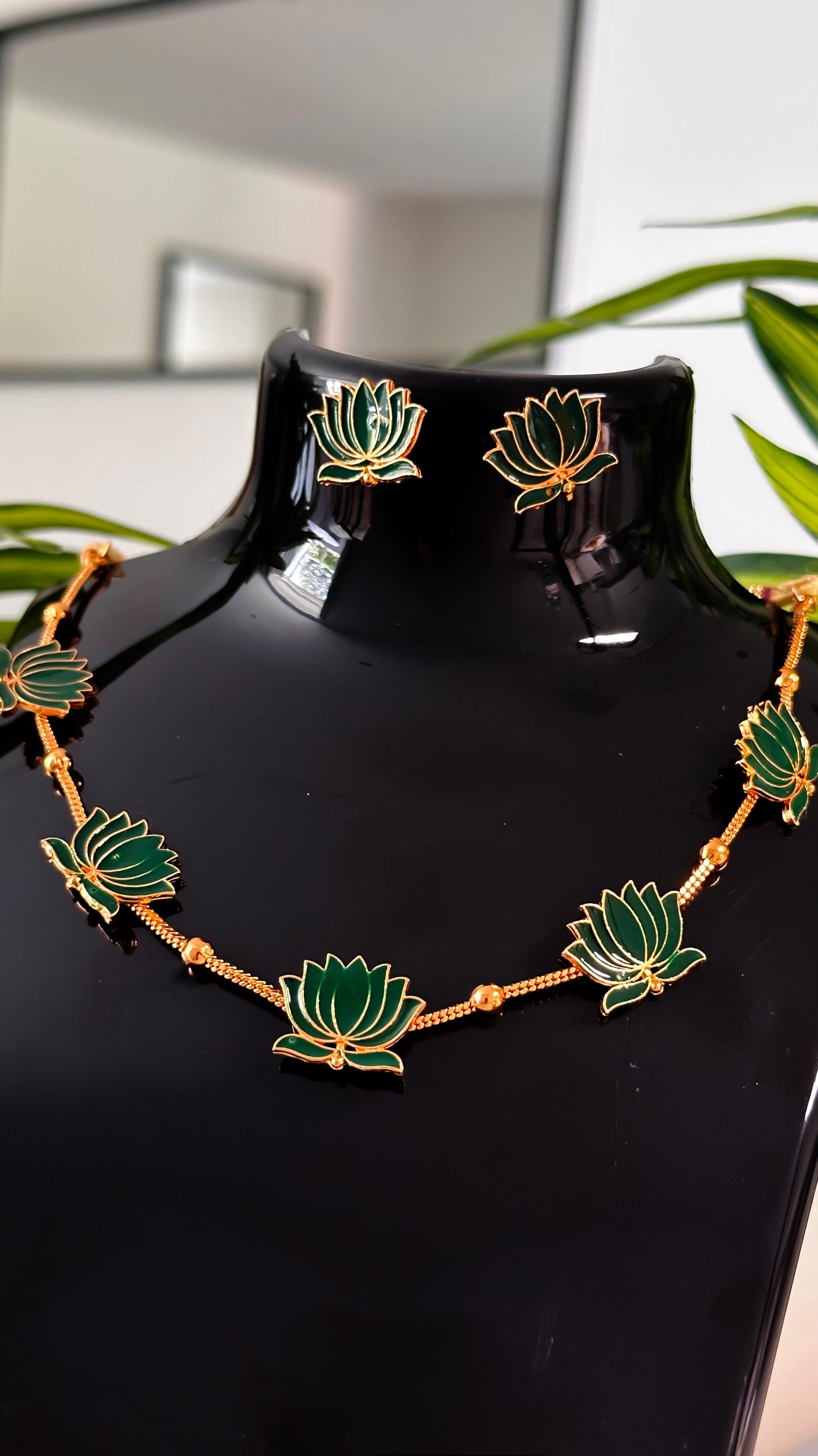 Green lotus enamel necklace with golden detailing and matching earrings on black display.