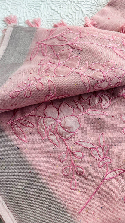Soft pink linen saree with floral appliqué embroidery, speckled pattern, grey border, and pink tassels.