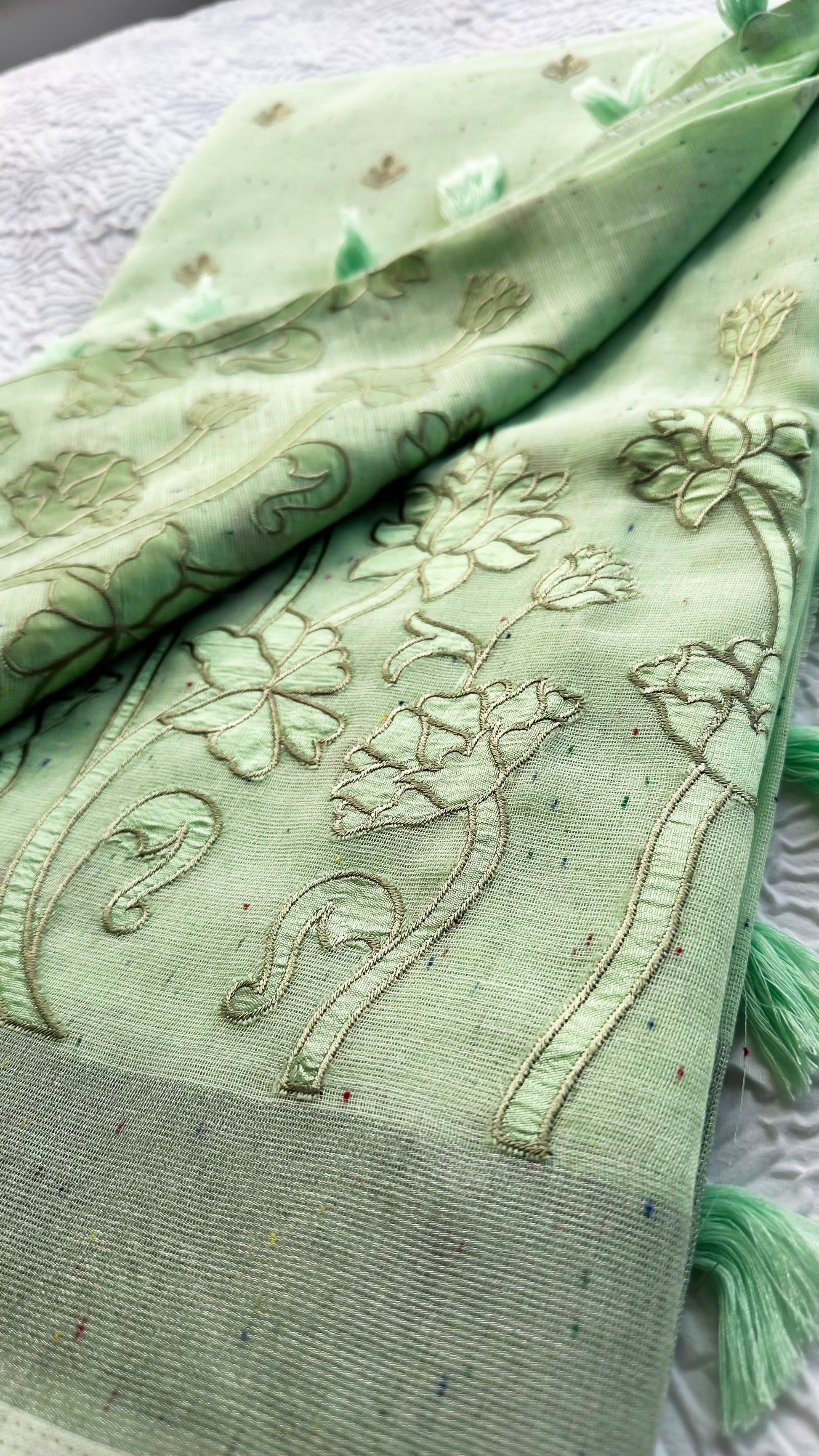 Light green linen saree with tonal floral appliqué embroidery and tassel pallu displayed on textured background.
