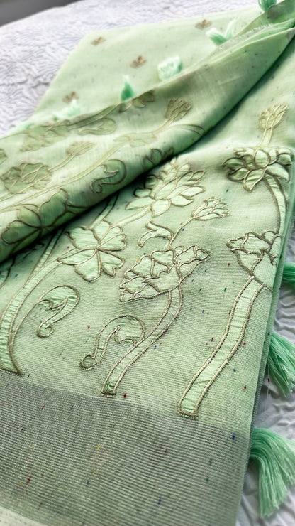 Light green linen saree with tonal floral appliqué embroidery and tassel pallu displayed on textured background.
