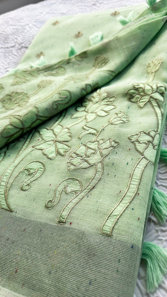 Light green linen saree with tonal floral appliqué embroidery and tassel pallu displayed on textured background.
