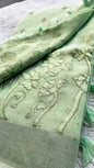 Light green linen saree with tonal floral appliqué embroidery and tassel pallu displayed on textured background.
