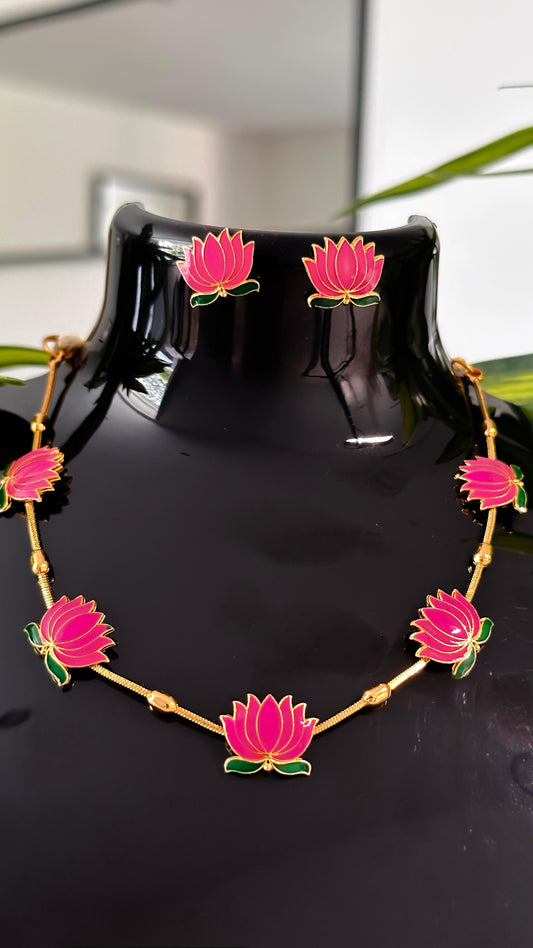 Pink lotus enamel necklace with golden beads and matching earrings on black display.
