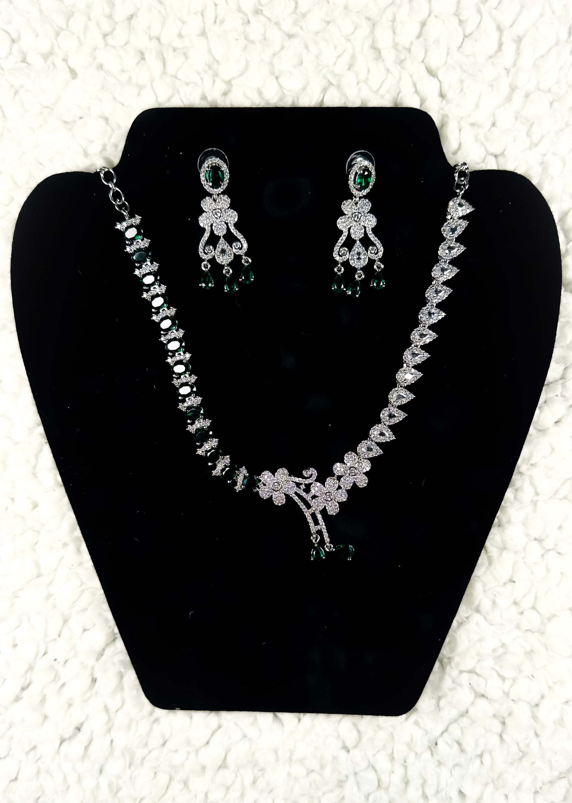 Silver crystal rhinestone necklace and earrings jewelry set with emerald green accent stones displayed on black velvet stand