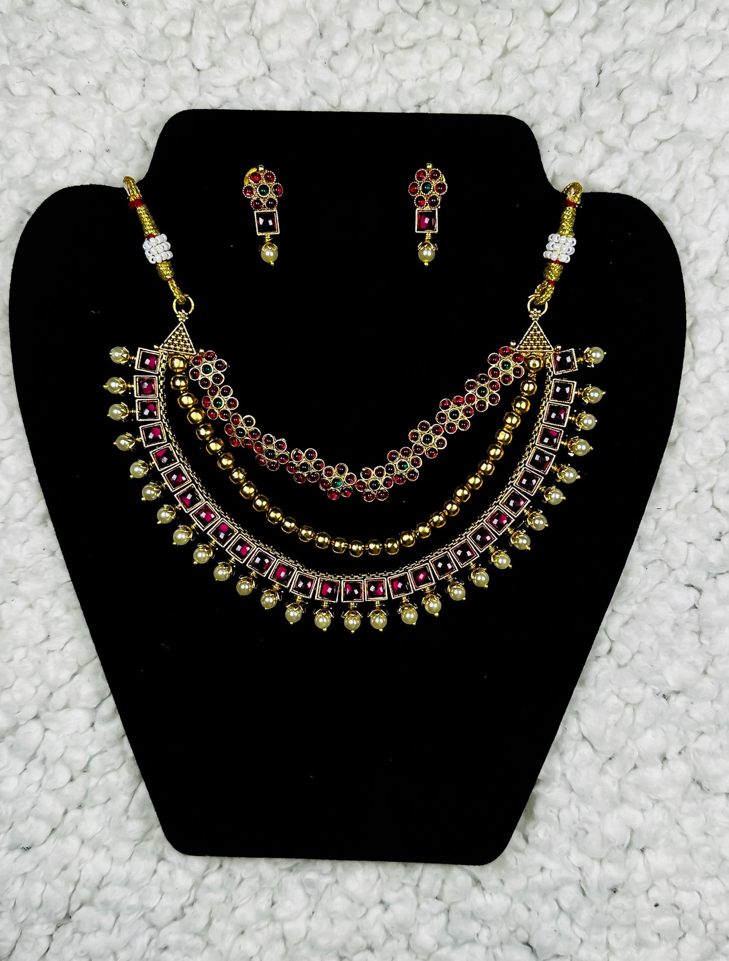 Traditional Indian bridal jewelry set with gold plated multi-layer necklace and ruby kundan earrings displayed on black velvet stand