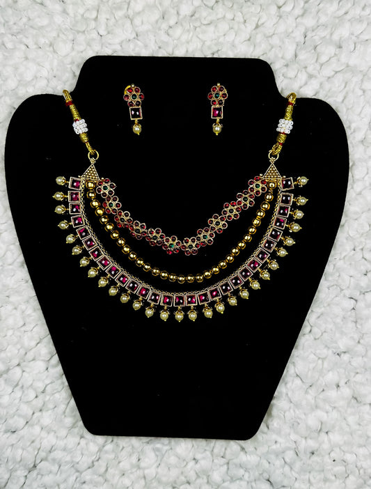 Traditional Indian bridal jewelry set with gold plated multi-layer necklace and ruby kundan earrings displayed on black velvet stand