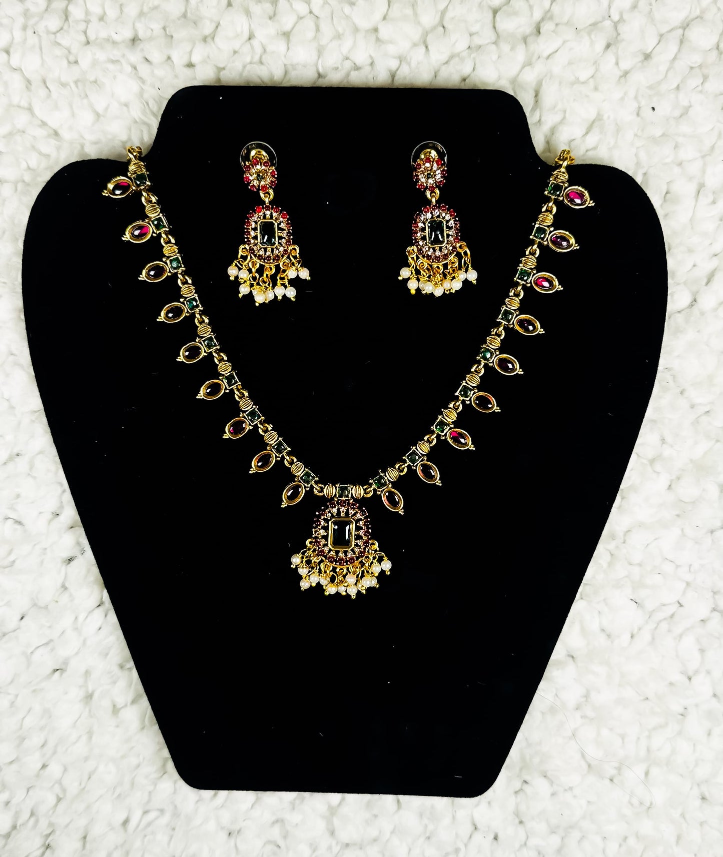 Traditional Indian gold chandbali necklace and earrings jewelry set with ruby stones pearl drops and kundan work in elaborate bridal design displayed on black velvet stand
