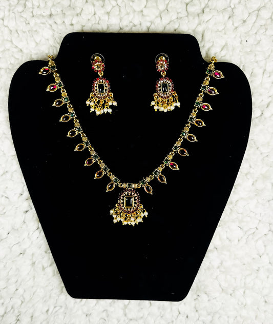 Traditional Indian gold chandbali necklace and earrings jewelry set with ruby stones pearl drops and kundan work in elaborate bridal design displayed on black velvet stand