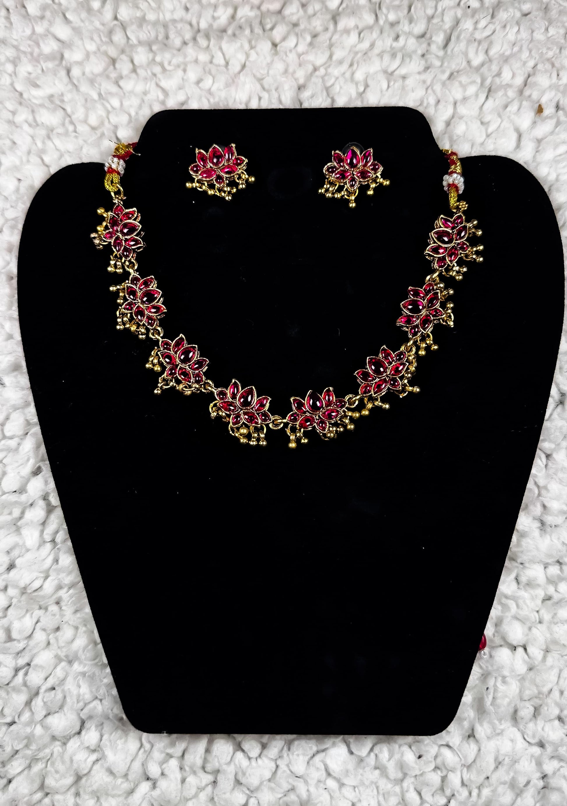 Traditional Indian gold lotus necklace and earrings jewelry set with ruby kundan work and spiritual lotus flower motifs displayed on black velvet stand