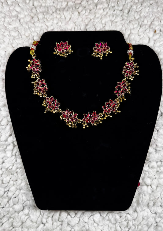 Traditional Indian gold lotus necklace and earrings jewelry set with ruby kundan work and spiritual lotus flower motifs displayed on black velvet stand