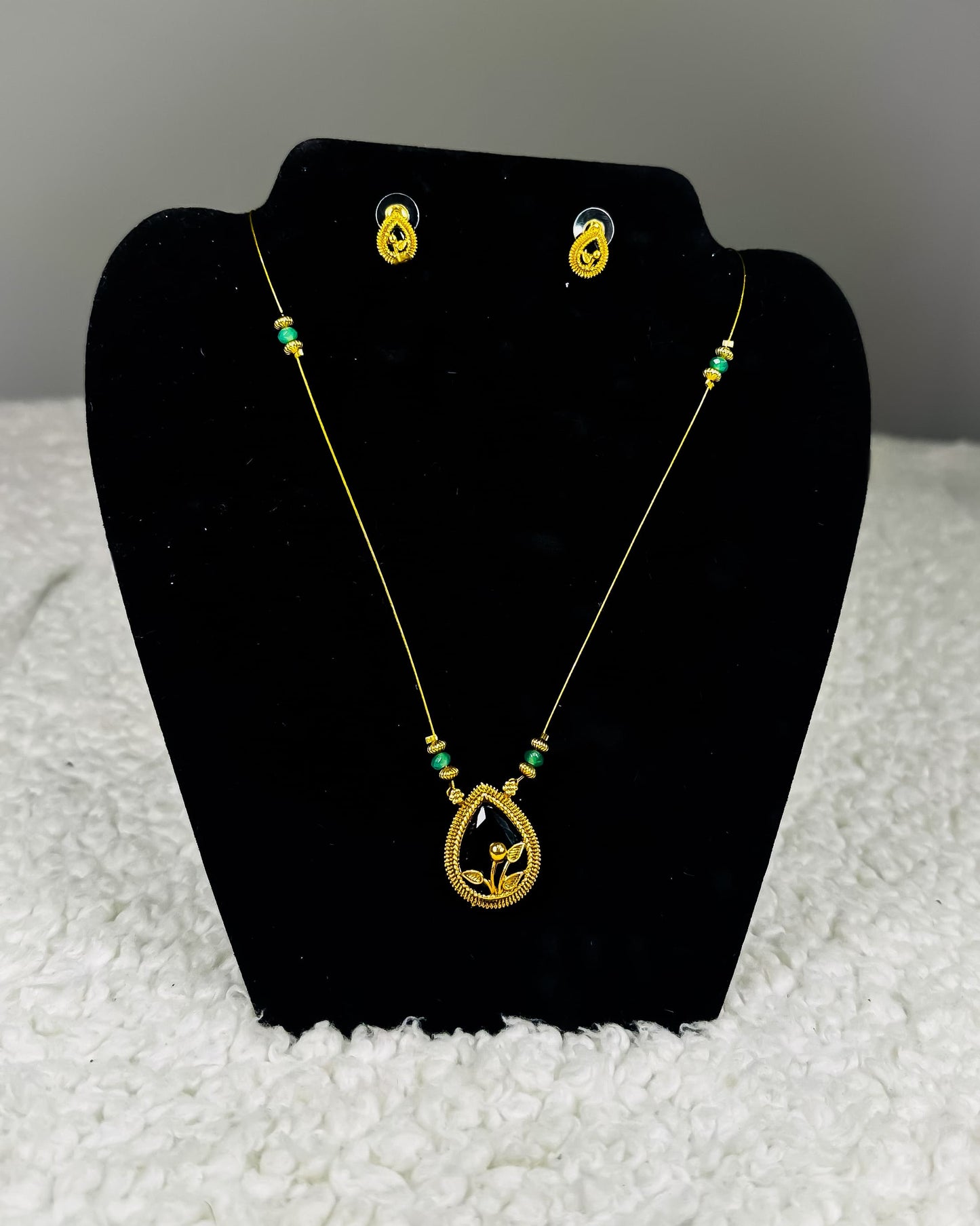 Traditional Indian gold thread necklace and earrings jewelry set with emerald green beads and paisley pendant showing authentic craftsmanship displayed on black velvet stand