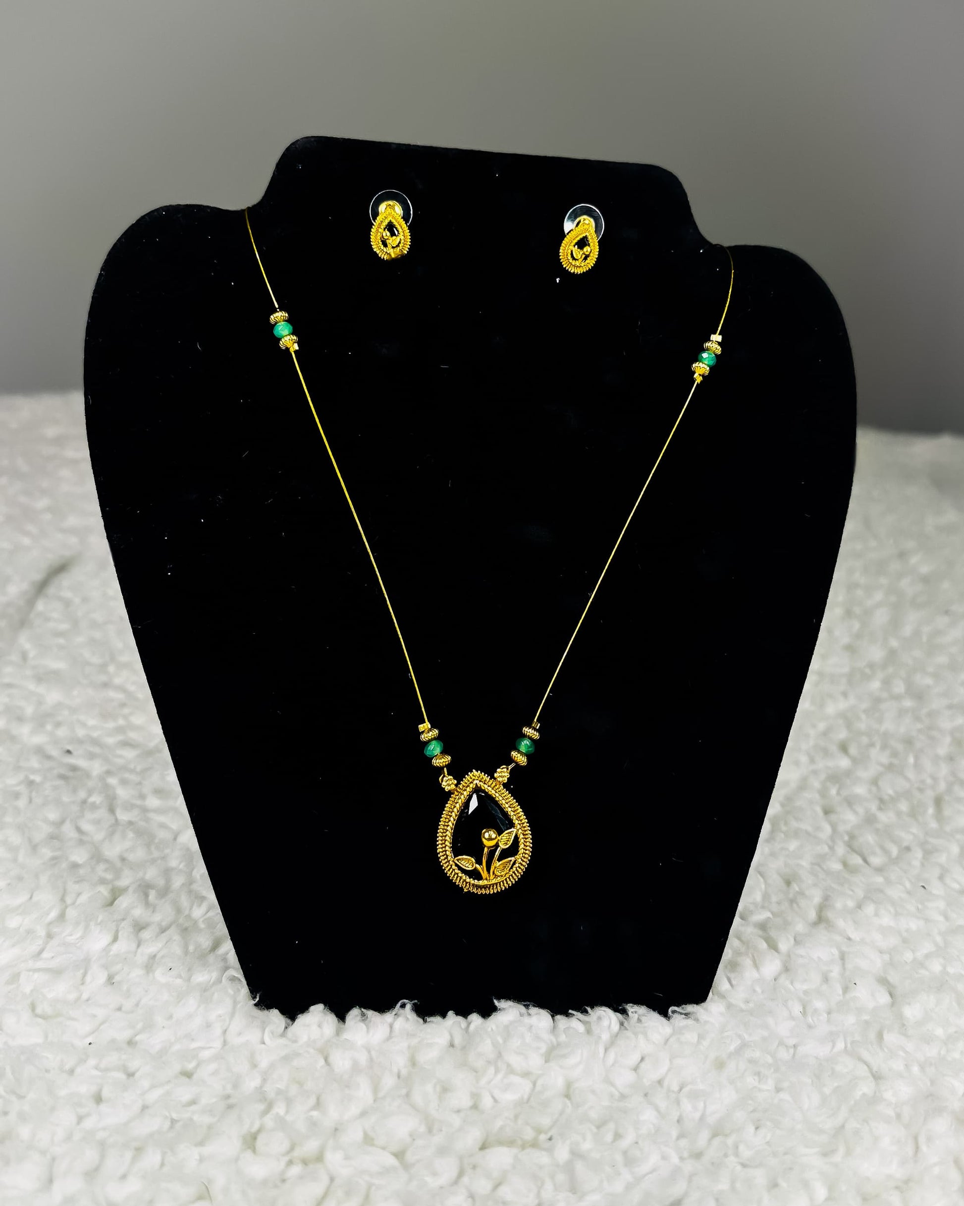 Traditional Indian gold thread necklace and earrings jewelry set with emerald green beads and paisley pendant showing authentic craftsmanship displayed on black velvet stand
