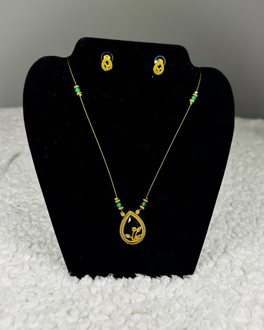 Traditional Indian gold thread necklace and earrings jewelry set with emerald green beads and paisley pendant showing authentic craftsmanship displayed on black velvet stand