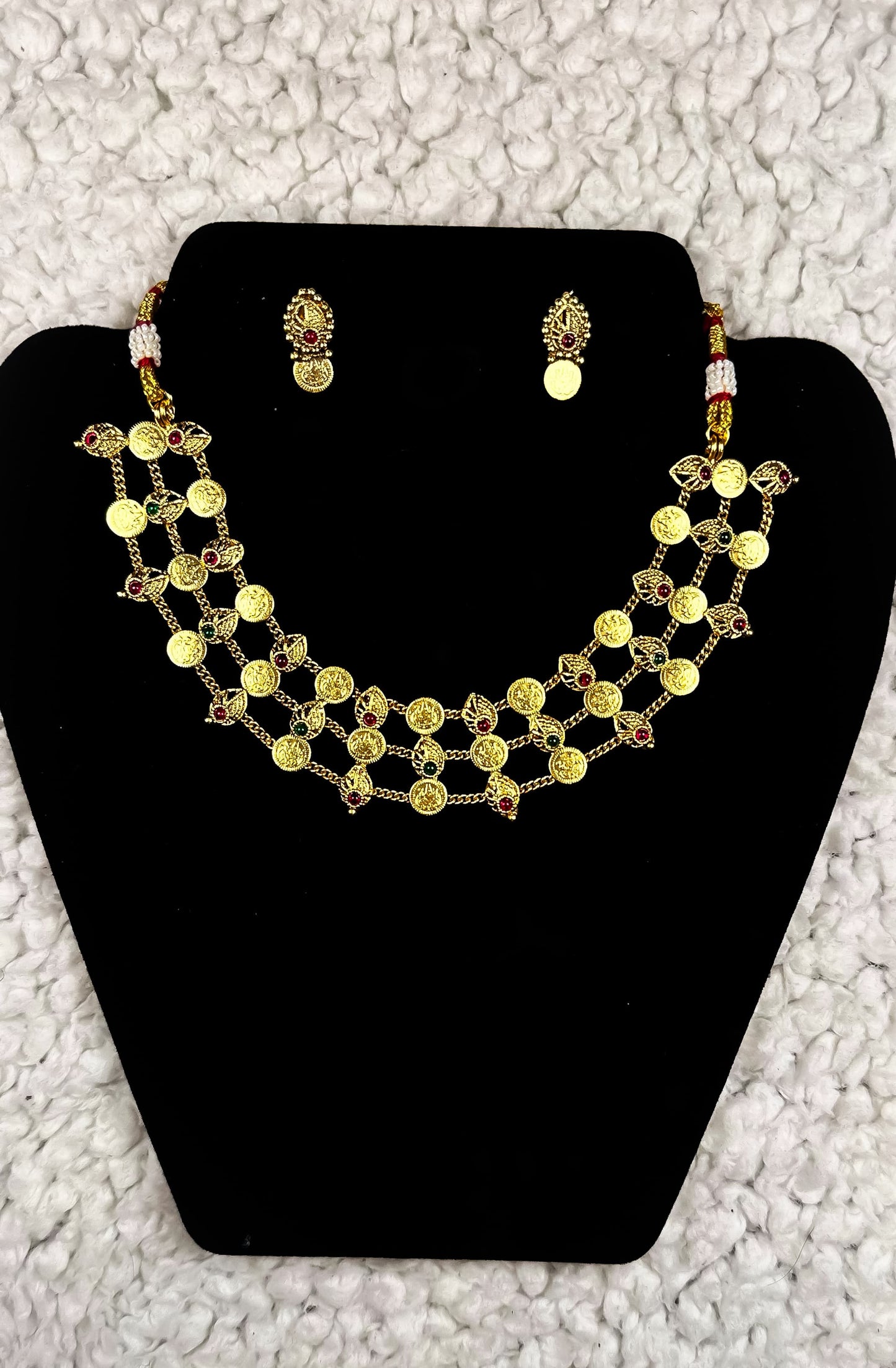 Traditional Indian multi-strand gold coin necklace and earrings jewelry set with temple motifs ruby accents and pearl details displayed on black velvet stand