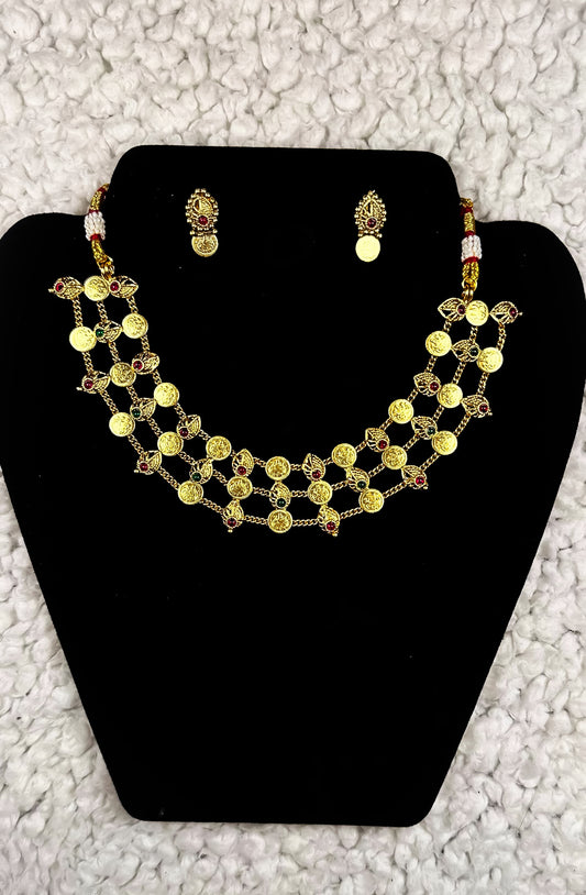 Traditional Indian multi-strand gold coin necklace and earrings jewelry set with temple motifs ruby accents and pearl details displayed on black velvet stand