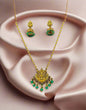 Traditional Indian temple jewelry set with gold Lakshmi pendant necklace and emerald green jhumka earrings displayed on black velvet stand